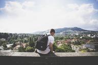 Male_with_Backpack_Sitting_on_Ledge_Overlooking_City.jpg